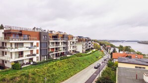 Un complex d'apartaments moderns amb balcons, un camí pavimentat i un riu amb un pont al fons.
