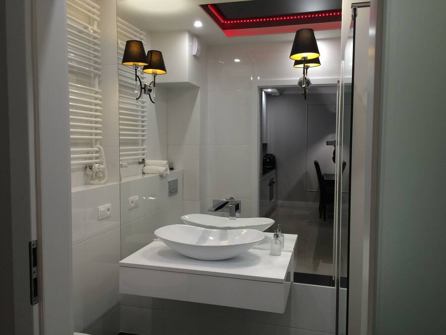 Un baño moderno con dos lavamanos blancos, un espejo grande y dos lámparas de pared.