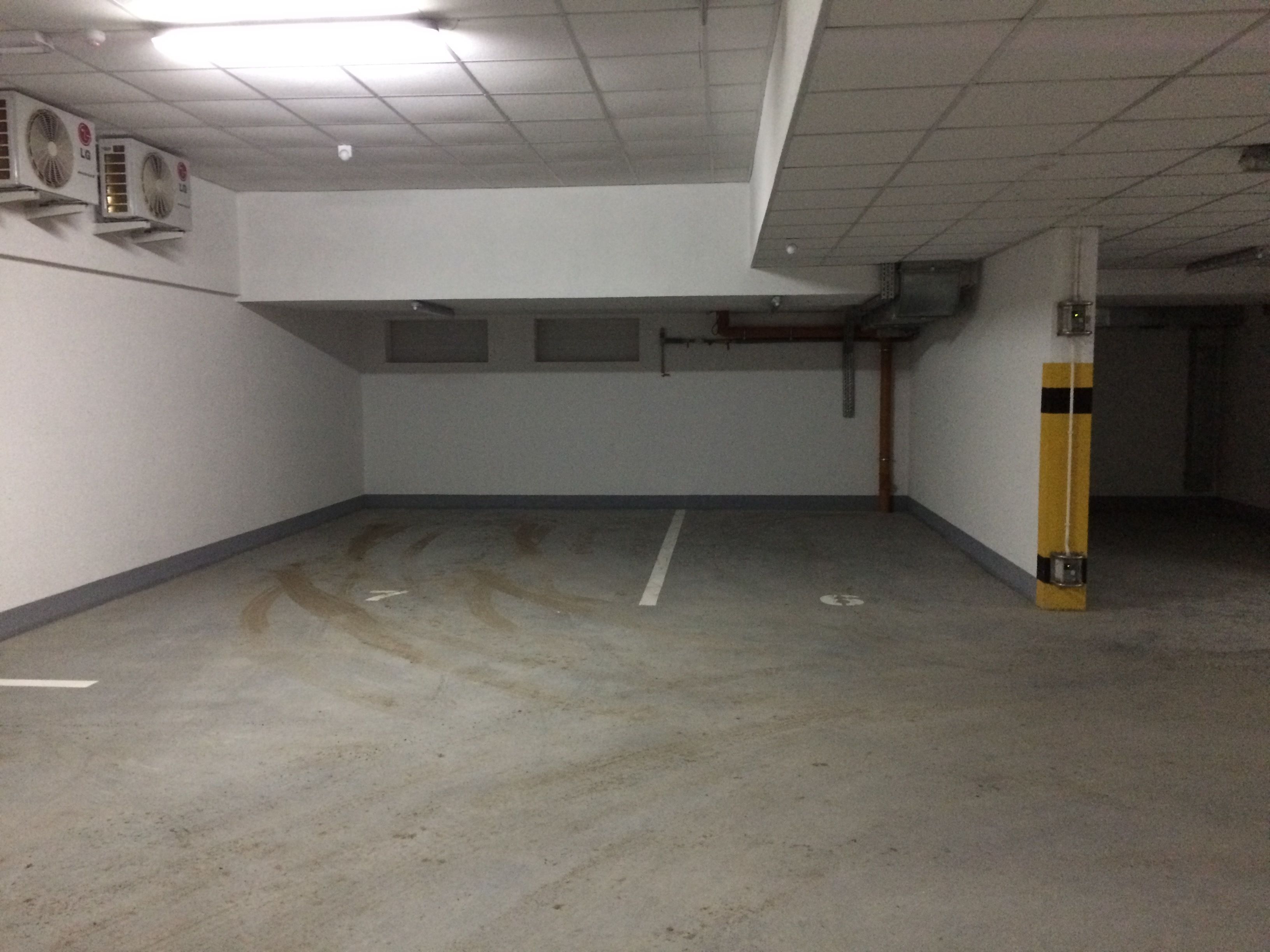 Een lege parkeergarage met betonnen vloeren, witte muren en airconditioningsunits aan het plafond.