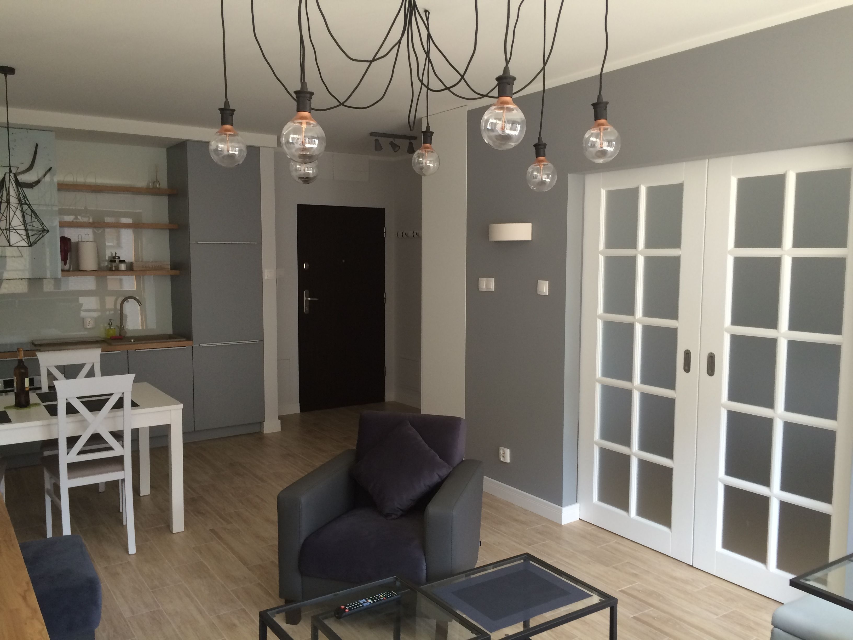 Una sala moderna con una mesa de centro de vidrio, un sillón oscuro y una zona de comedor con una mesa y sillas blancas.