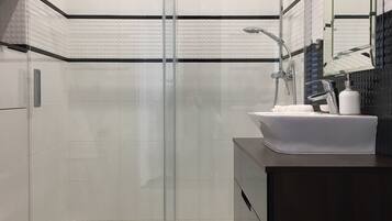 A modern bathroom with a glass-enclosed shower, a white sink, and a dark vanity.