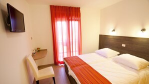 Ein Hotelzimmer mit Bett, Sessel, kleinem Tisch mit Vase und Wandfernseher.