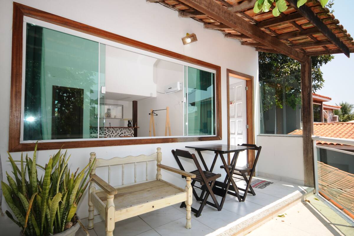 Un balcón con un banco de madera, dos sillas y un ventanal con vistas a una cocina.