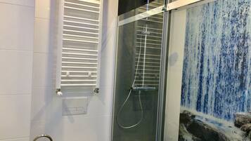 A modern bathroom with a glass-enclosed shower, a white towel rack, and a decorative wall with a blue and white pattern.