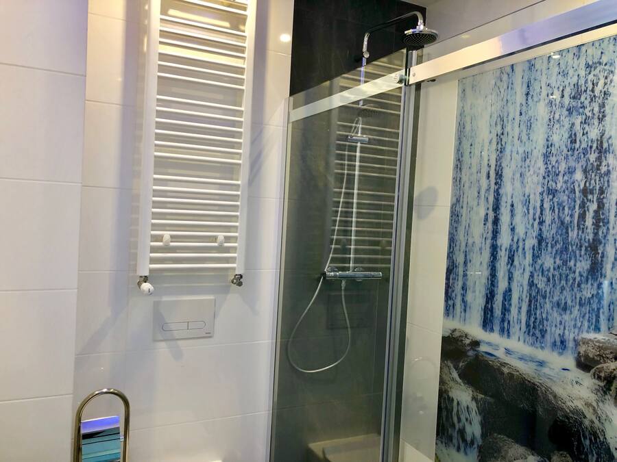 A modern bathroom with a glass-enclosed shower, a white towel rack, and a decorative wall with a blue and white pattern.