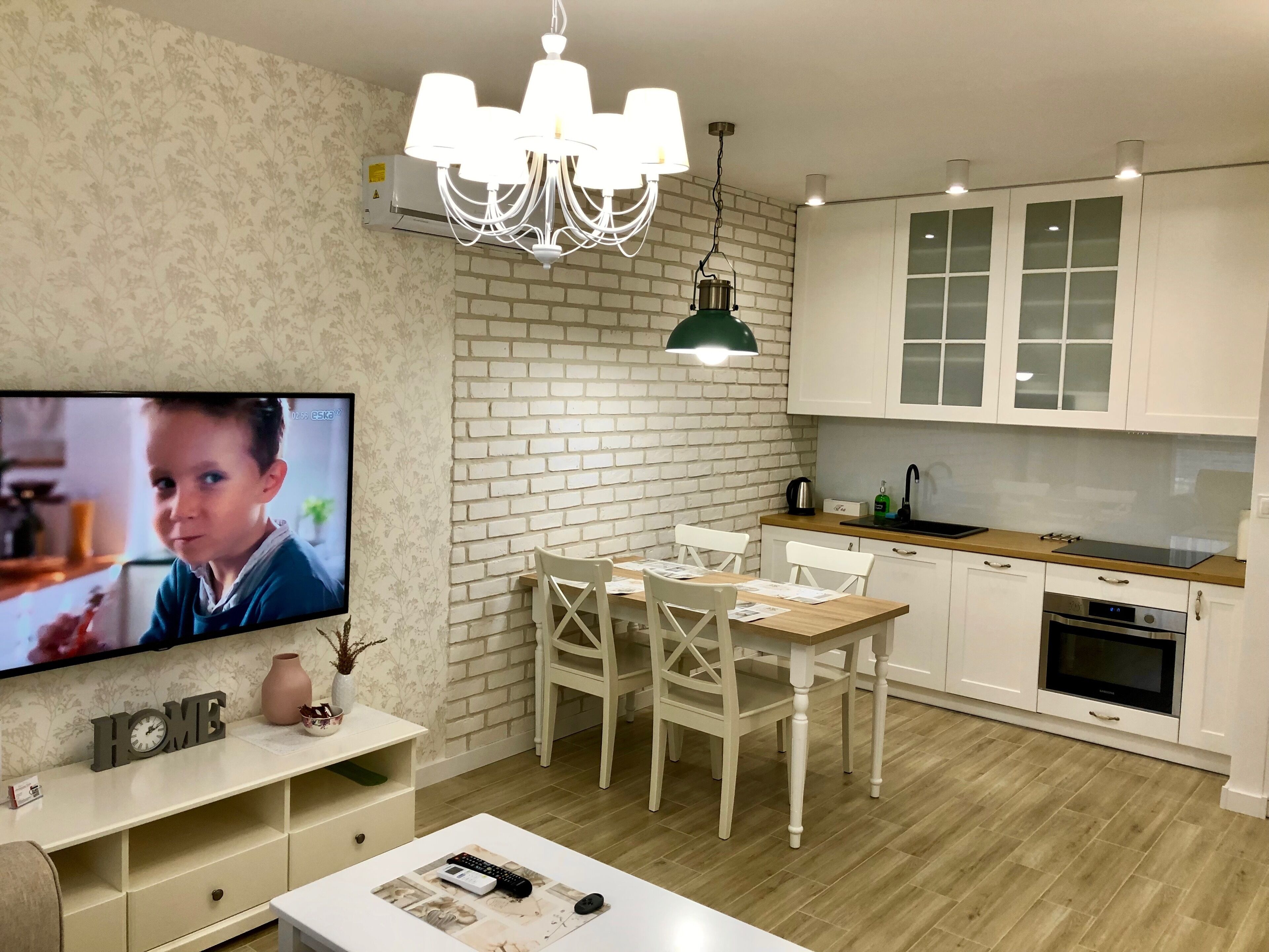 Une cuisine moderne avec des armoires blanches, un mur d’accent en briques et un coin repas comprenant une table et des chaises en bois.