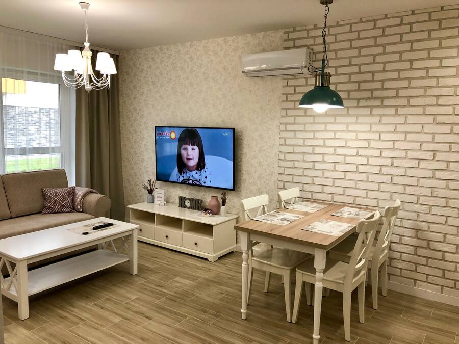A modern living room with a sofa, coffee table, TV, and dining table with chairs.