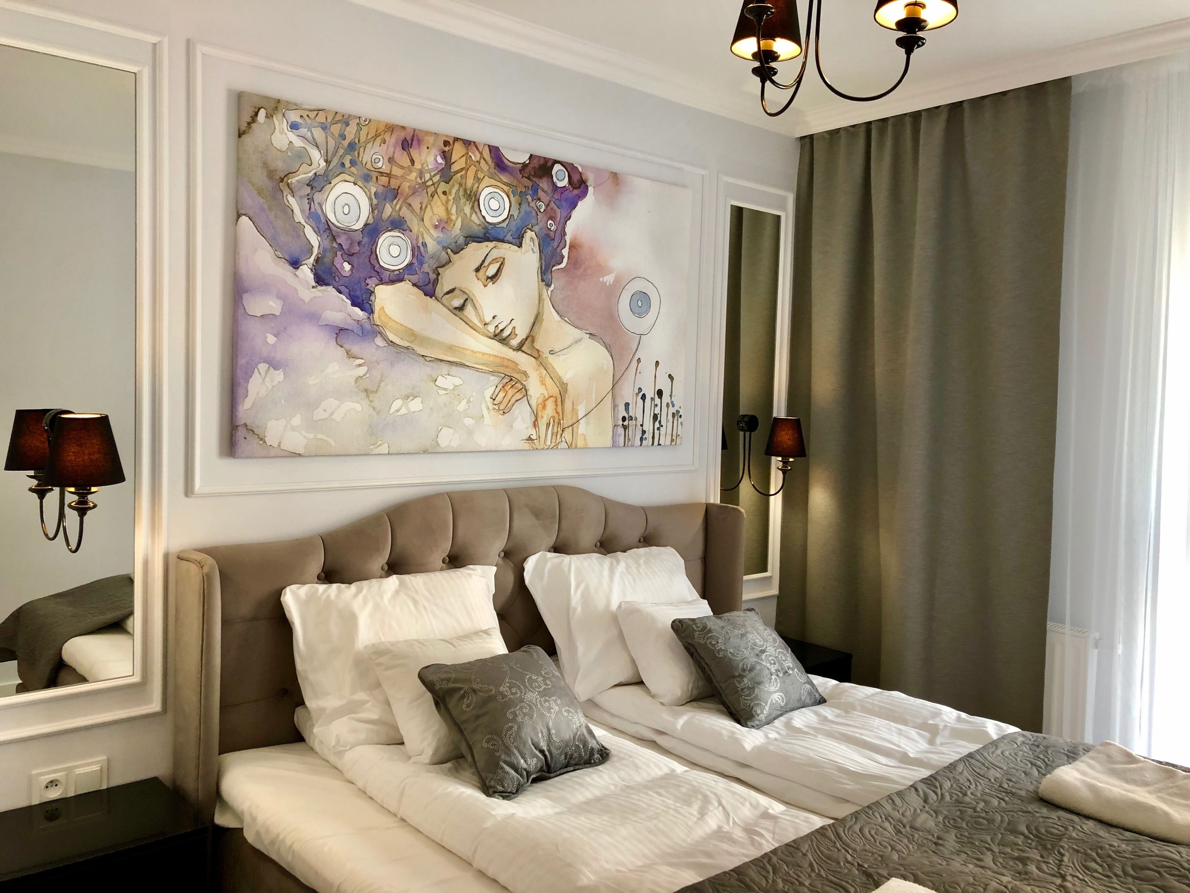 Un dormitorio con una cama grande, dos lámparas de noche, un cuadro sobre la cama y una ventana con cortinas.