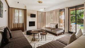 A spacious living room with a large sofa, a coffee table, and a TV mounted on the wall. There is a sliding glass door leading to an outdoor area with a pool. - Villa de Luxe Domaine des Kasbahs C5 (Marrakech)