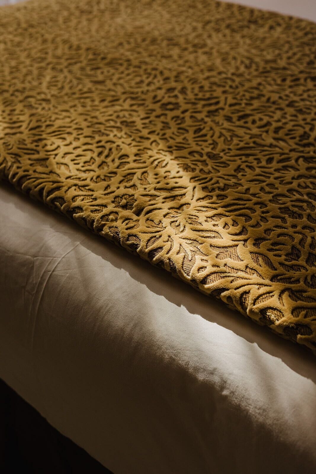 A bed with a patterned bedspread and a plain pillow.