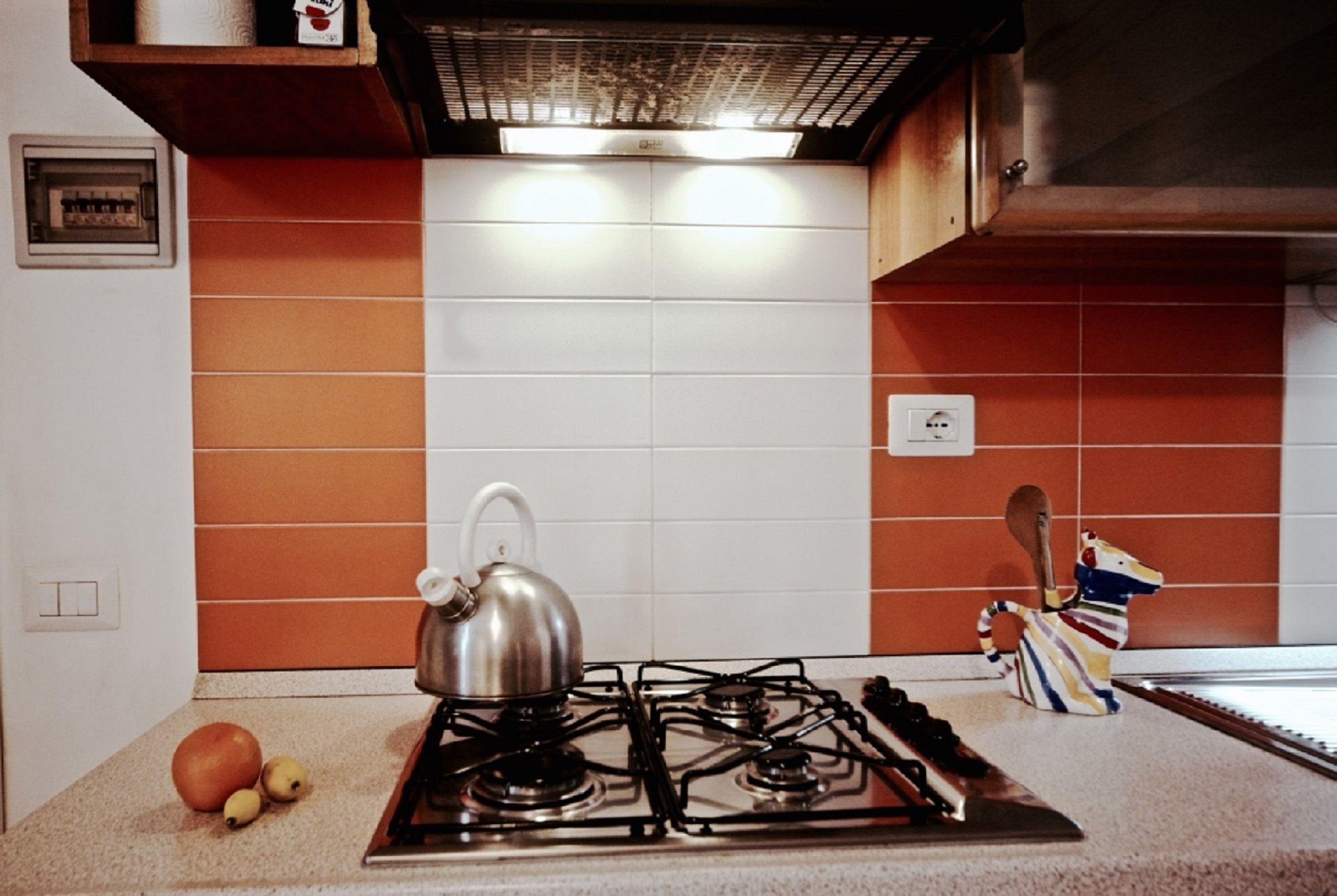 A kitchen with a gas stove, a kettle, and a colorful kitchen utensil holder.