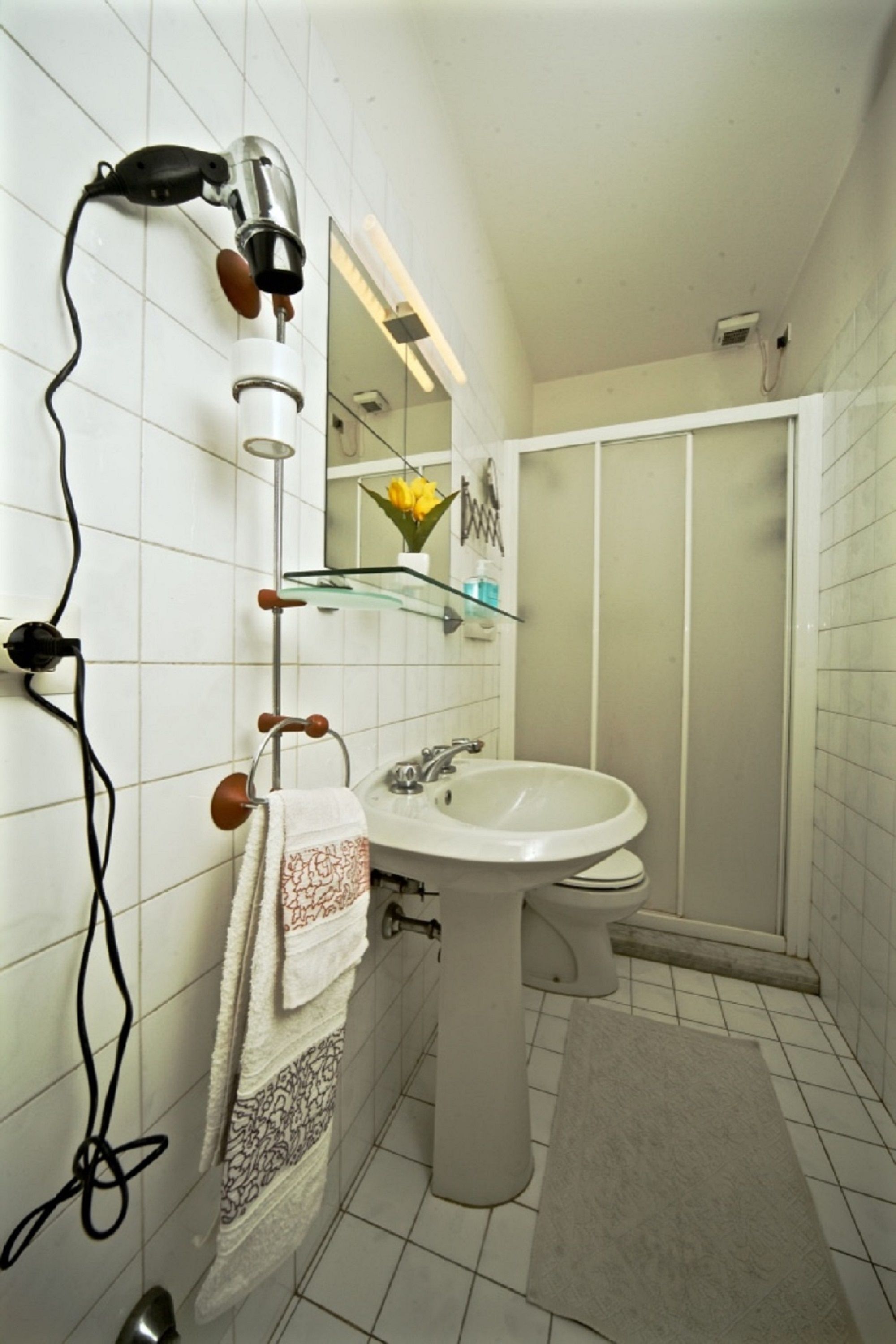 A bathroom with a white sink, a glass shelf, a towel rack, and a hairdryer.