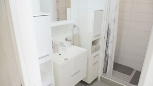 A white bathroom with a sink, mirror, and shower. - B Apartment (Ljubljana)