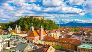 A panoramic view of a historic town with a prominent castle on a hill, surrounded by colorful buildings and a clear sky. - B Apartment (Ljubljana)