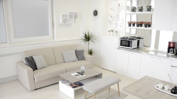 A modern living room with a sofa, coffee table, and bench. There is a kitchen area with a microwave and cabinets. - B Apartment (Ljubljana)