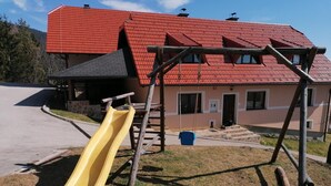 A playground with a yellow slide and swings, set against a building with a red roof and beige walls. - Guest House Koprivnik (Zrece)