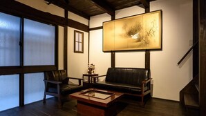 A traditional Japanese-style room with tatami flooring, a black leather sofa, a wooden coffee table, and a large framed artwork on the wall. - Gojo Samurai Machiya, Gojo Samurai Machiya (Kyoto)