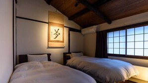 A room with two beds, wooden beams on the ceiling, a large window with curtains, and a hanging sign with Japanese characters. - Gojo Samurai Machiya, Gojo Samurai Machiya (Kyoto)