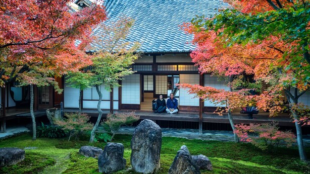 A traditional Japanese building with a tiled roof and wooden structure, surrounded by a garden with rocks and autumn-colored trees. - Gojo Samurai Machiya, Gojo Samurai Machiya (Kyoto)