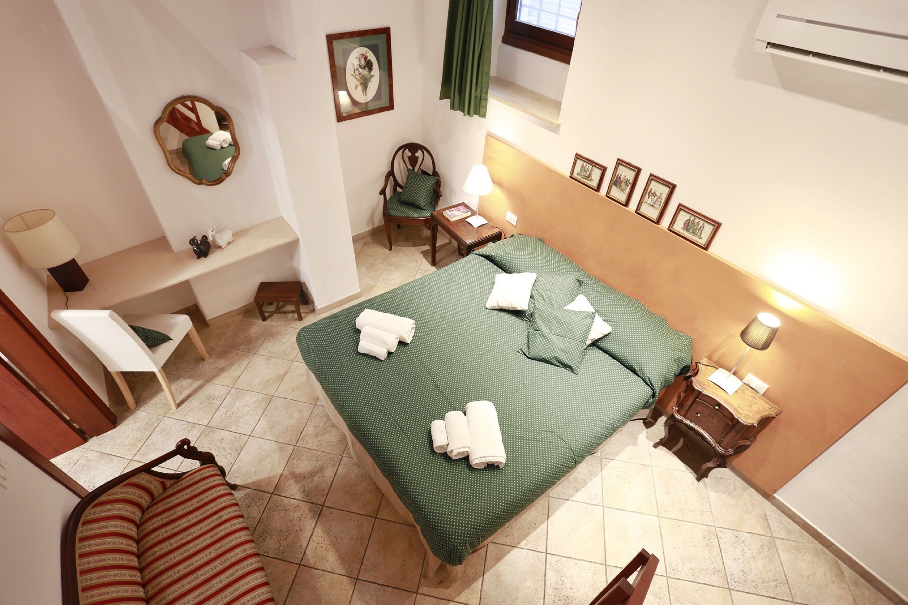 A hotel room with a large bed, a chair, a small table, a desk, a mirror, and a window with curtains.