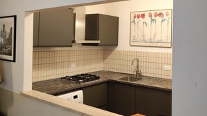 A compact kitchen with a gas stove, a sink, and dark cabinets. A framed picture of flowers hangs on the wall above the sink. - Ghibellina Apartment (Florence)