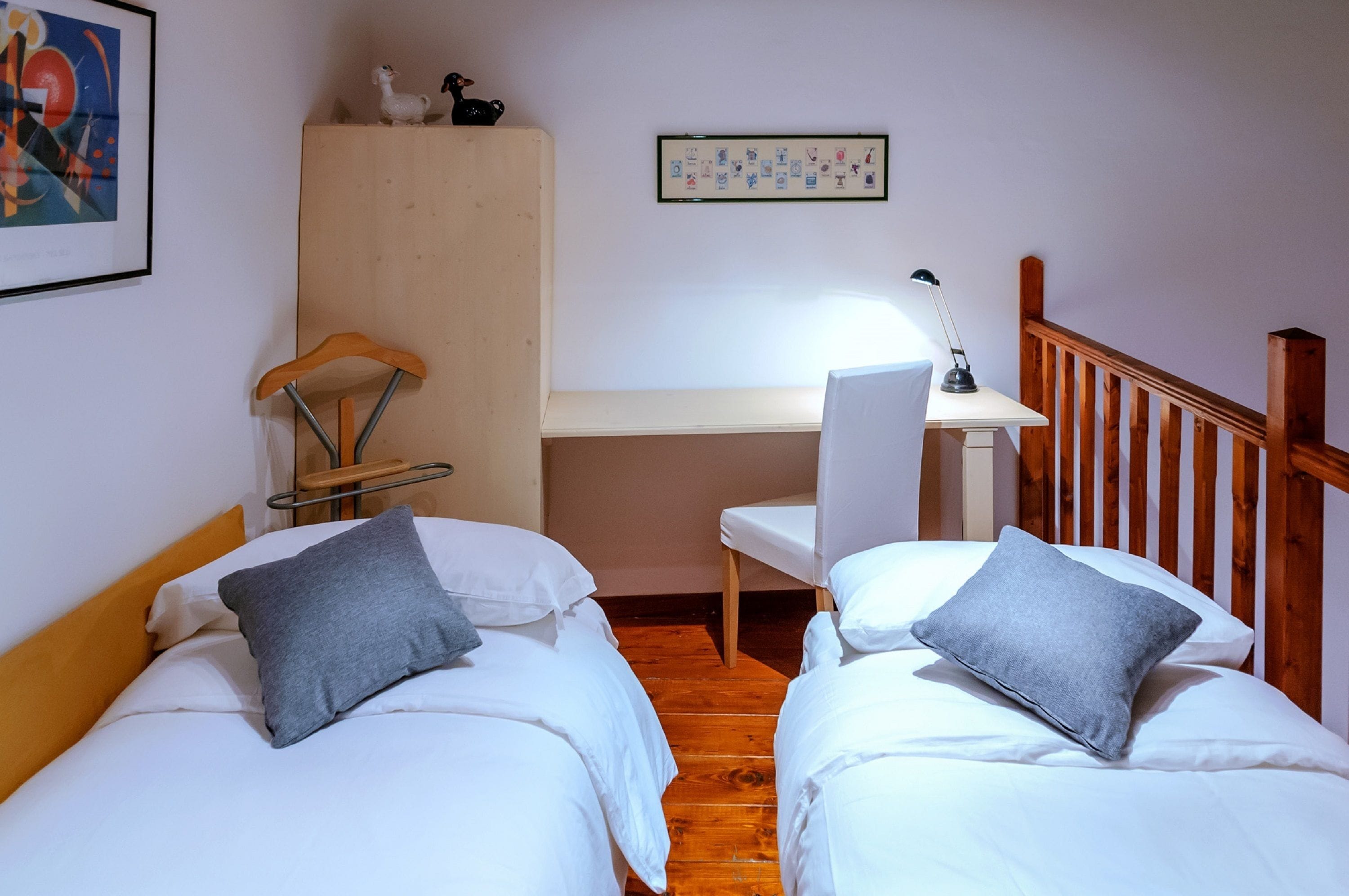 A bedroom with two single beds, a wooden desk, a chair, and a small shelf with decorative items.