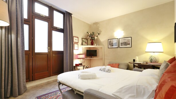 A hotel room with a large bed, a sofa, a TV, a desk, and a window with curtains. - Ghibellina Apartment (Florence)