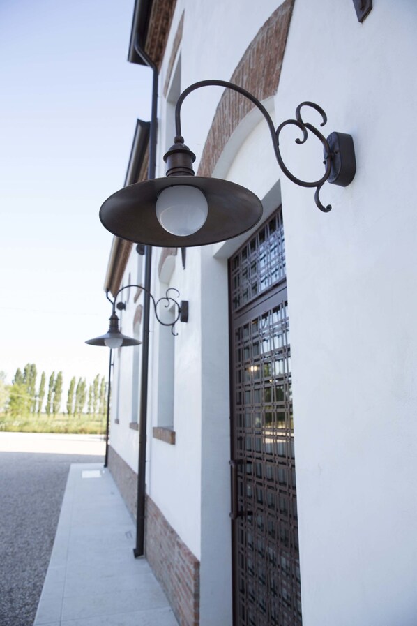Un edificio con fachada blanca, una verja metálica y dos luces fijadas en la pared.