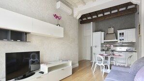 Una sala de estar moderna con un televisor de pantalla plana, muebles blancos, un comedor y una cocina.