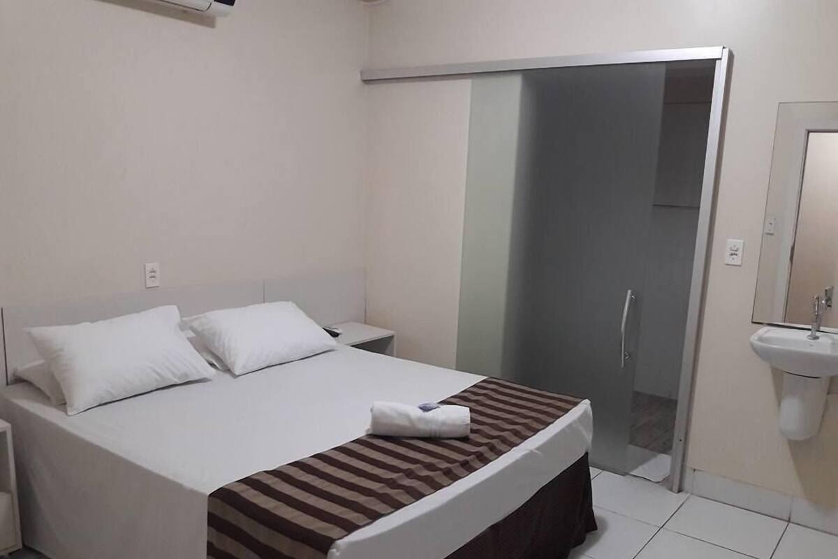 A hotel room with a bed, a nightstand, a bathroom with a sink, and a sliding door to a shower area.