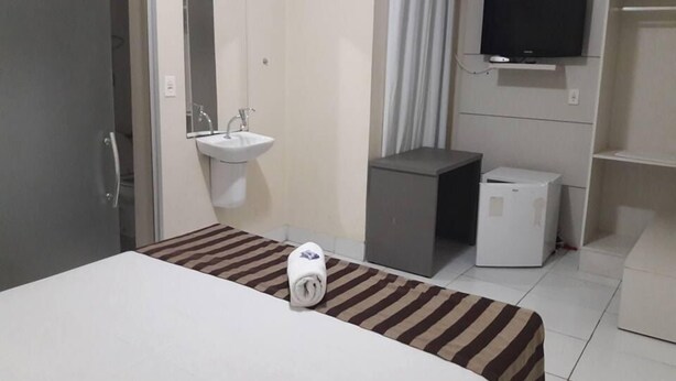 A hotel room with a bed, a sink, a television, and a small refrigerator. - Hotel Express (Varzea Grande)