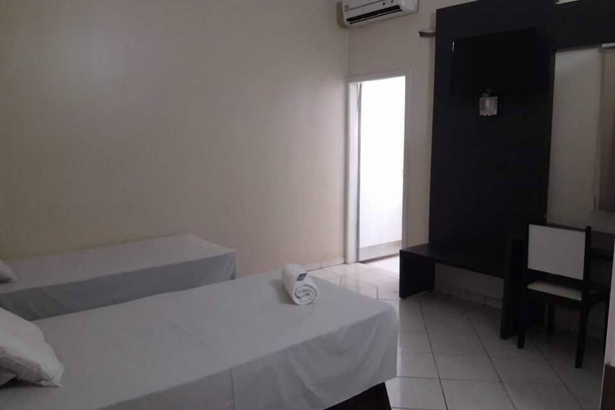 A hotel room with two single beds, a desk, a chair, and an air conditioning unit.