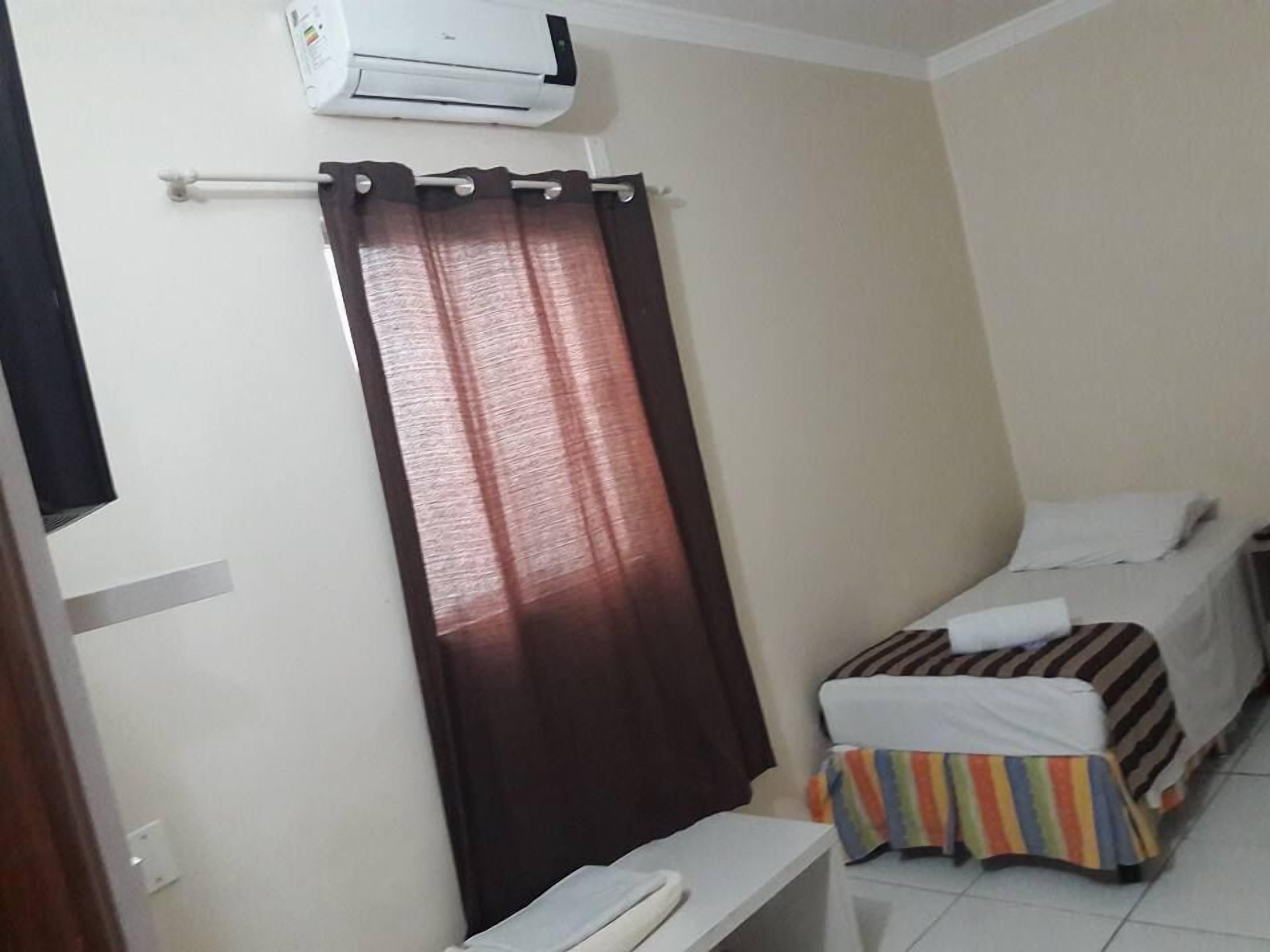 Une petite chambre propre, avec deux lits simples, une petite table et un rideau.