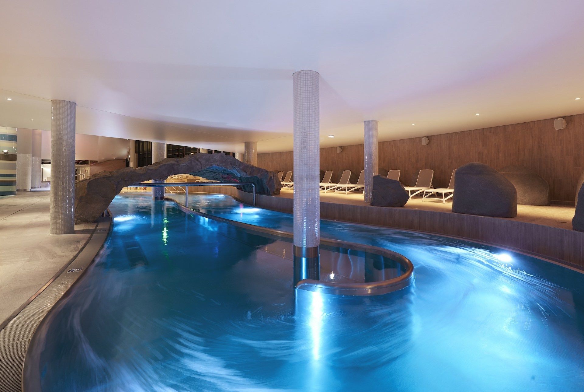 Piscina com escorrega, espreguiçadeiras e uma parede de madeira.