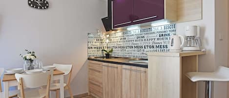 A modern kitchen with wooden cabinets, a black clock, and a coffee machine.