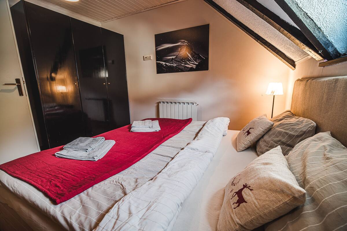 Ein Hotelzimmer mit einem Bett, einer roten Decke, einem Kissen mit einem Hirschmotiv, einem Wandbild eines Vulkans und einer Heizung.