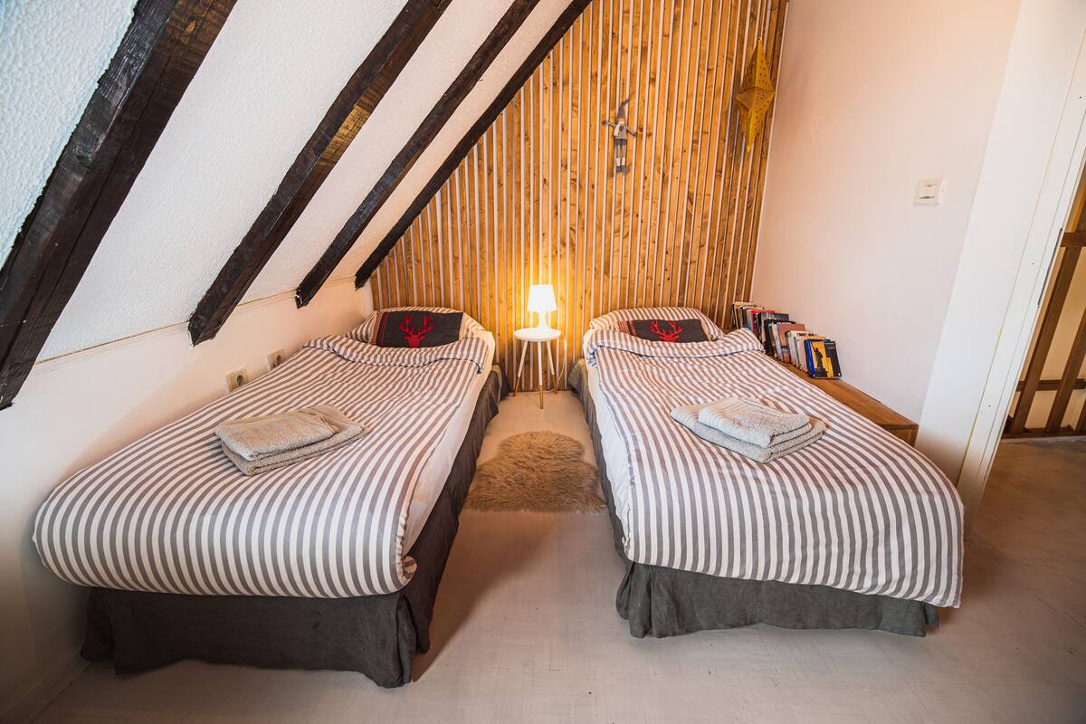 Ein gemütliches Zimmer mit zwei Betten, einem kleinen Tisch mit Lampe und einem Bücherregal.