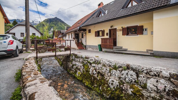 A quaint village street with stone walls, a small bridge, and houses with wooden shutters. - Apartments Wanderlust (Bovec)