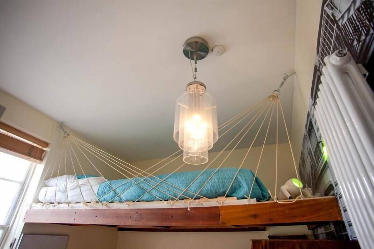 A hammock bed suspended from the ceiling with a hanging light fixture above it.