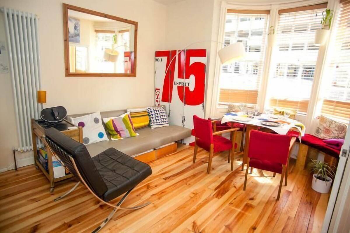 A compact living space with a sofa, a dining table, and a chair. A large number '75' is visible on the wall.