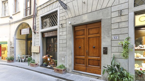A building with a large wooden door, potted plants, and outdoor seating. - Lambertesca il Cuore di Firenze (Florence)