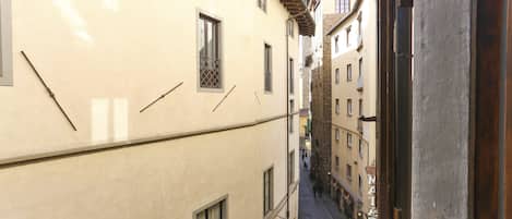A narrow street with buildings on either side, featuring balconies and a clear sky.