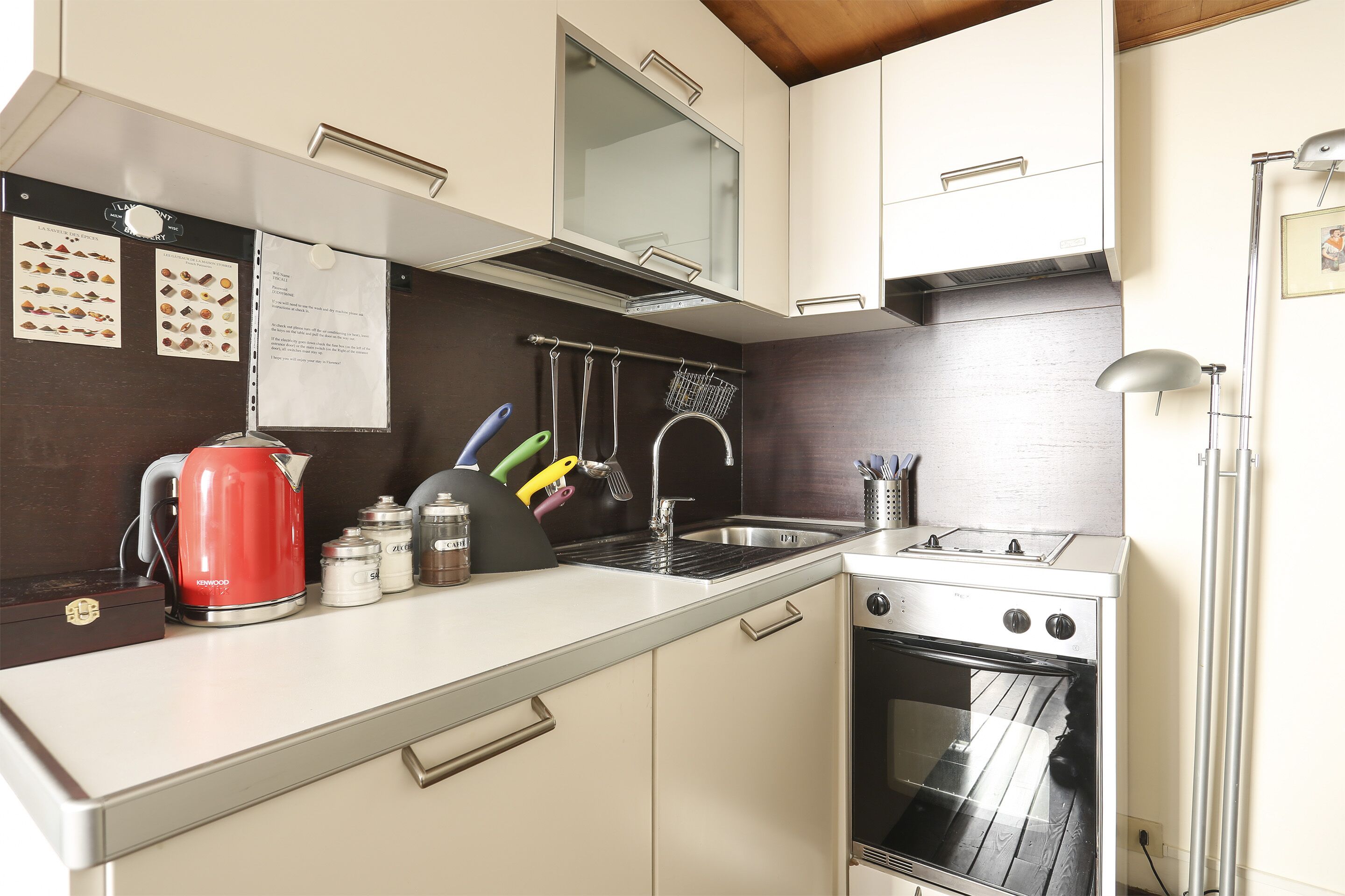 A kitchen with white cabinets, a red kettle, a stove, and a sink.