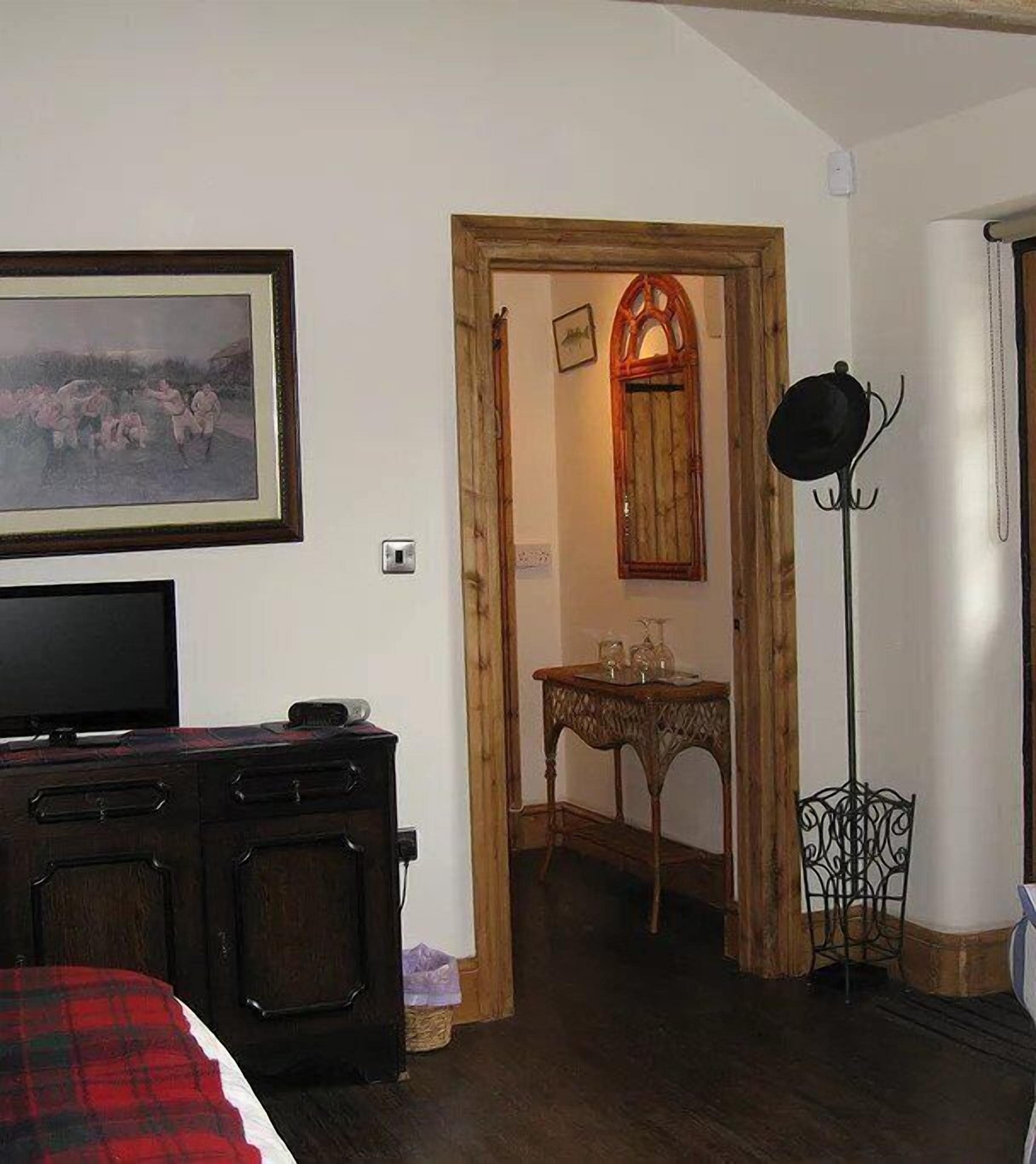 Una stanza con un letto, una TV, una cassettiera in legno, un tavolo con bicchieri e un appendiabiti.