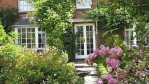 Een klassiek bakstenen huis met een tuinkamer, omringd door weelderige begroeiing en bloeiende planten.