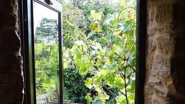 Een doorgang naar een tuin met een houten bankje en een stenen muur.