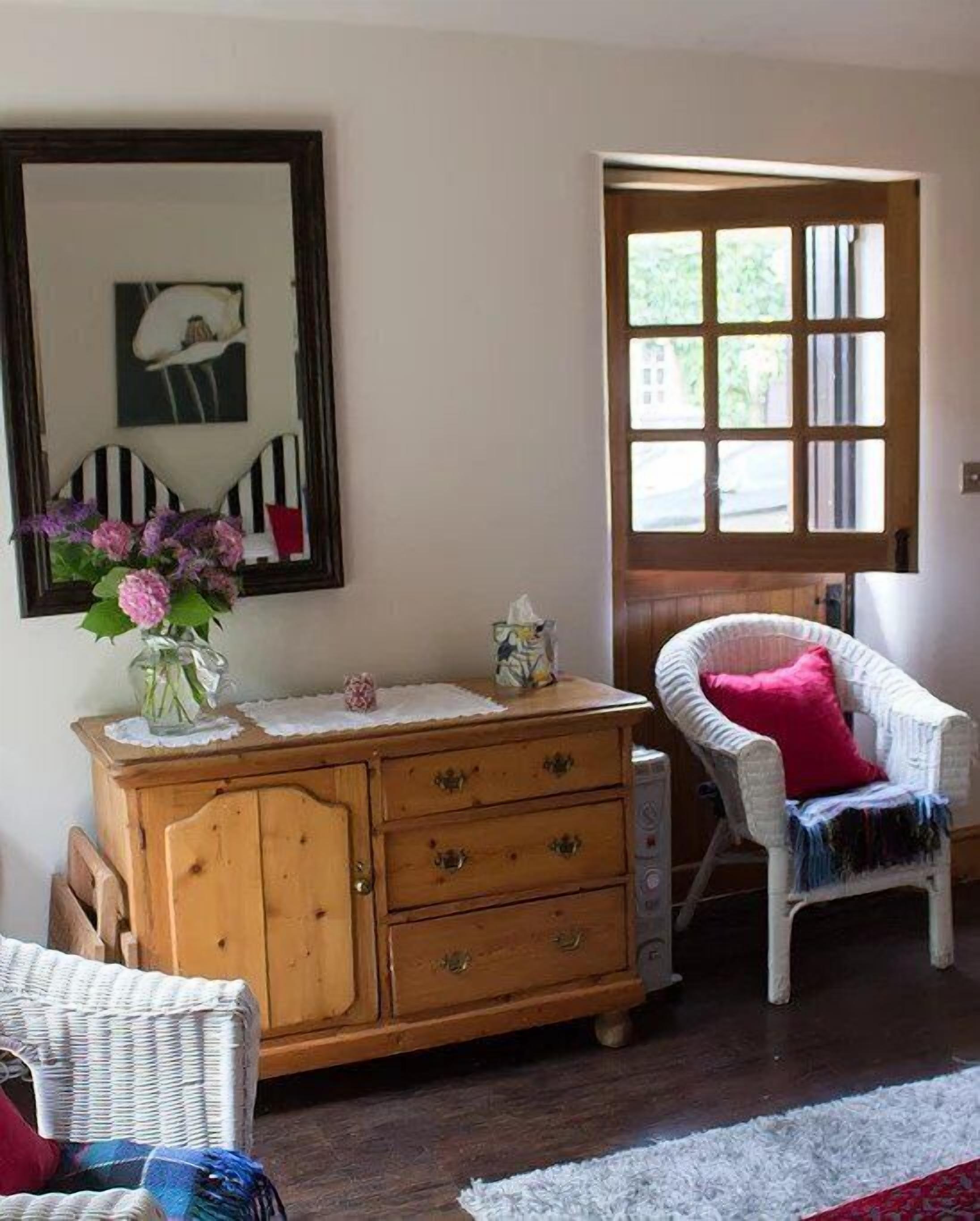 Una habitación acogedora con un aparador de madera, una silla de mimbre y un ventanal grande.