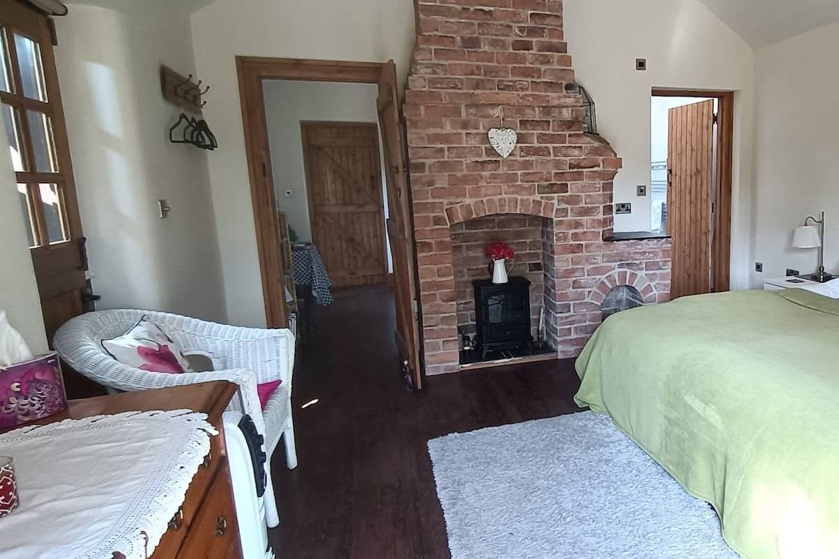 Een slaapkamer met een bakstenen openhaard, een bed met gestreept hoofdeinde en een rieten stoel.