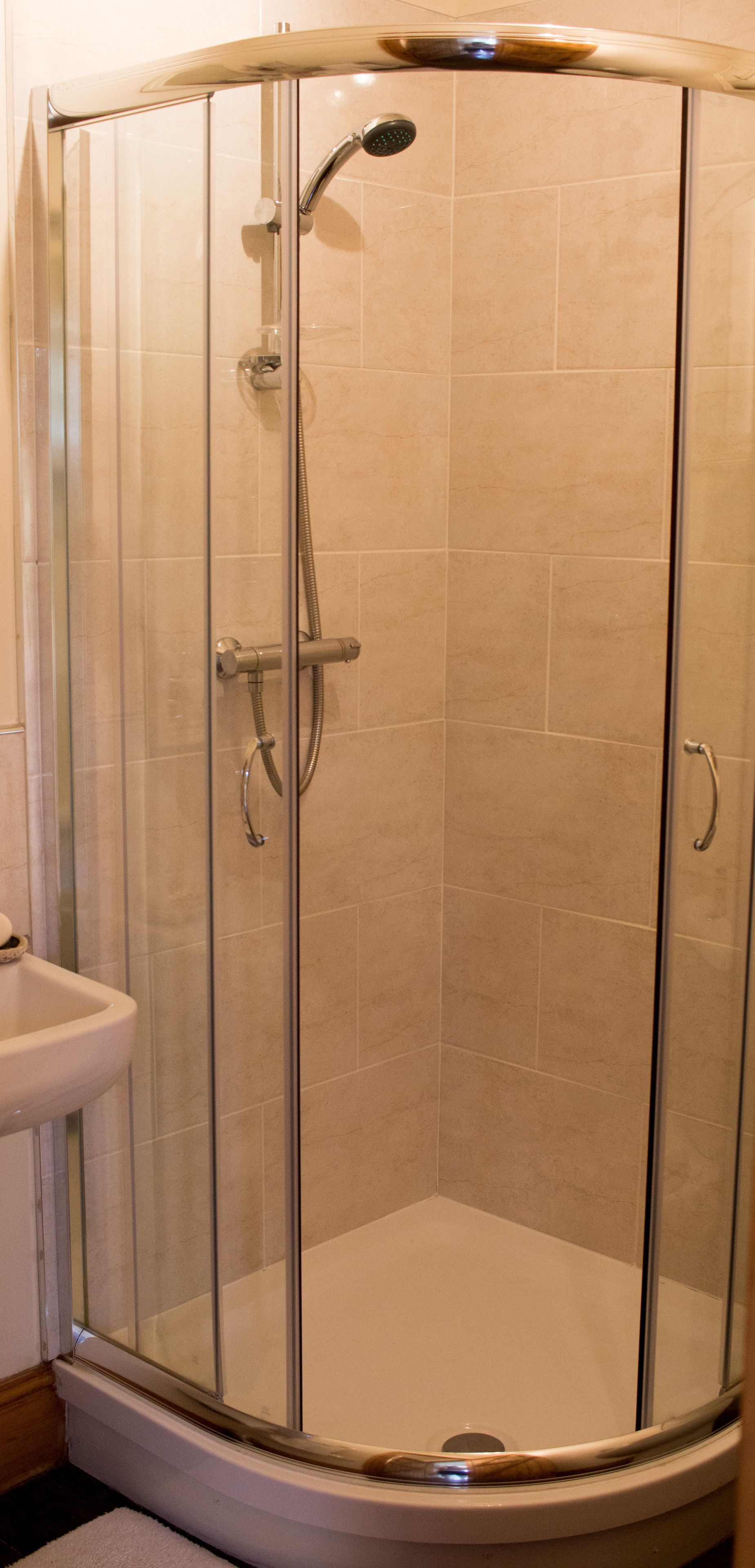 A glass-enclosed shower with a handheld showerhead and a wall-mounted faucet.