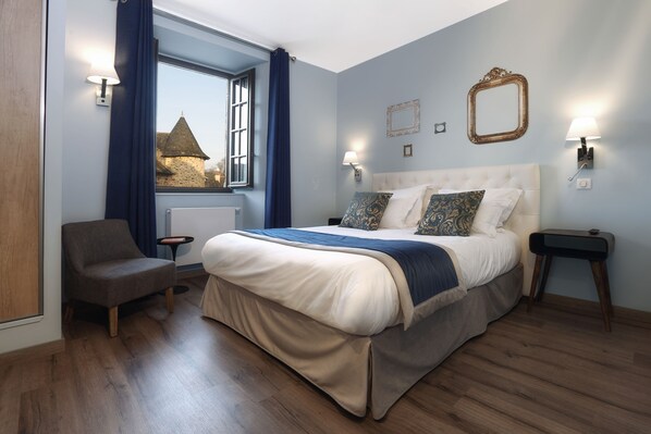 A bedroom with a large bed, a chair, a nightstand, and a window with curtains. - Hôtel Joyet de Maubec (Uzerche)